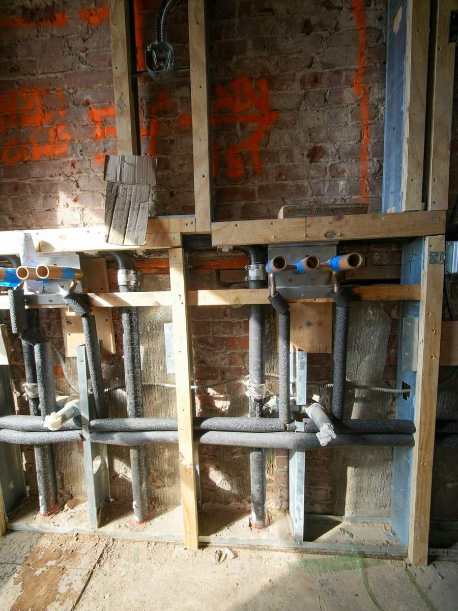Exposed plumbing pipes and electrical conduit inside a wall
