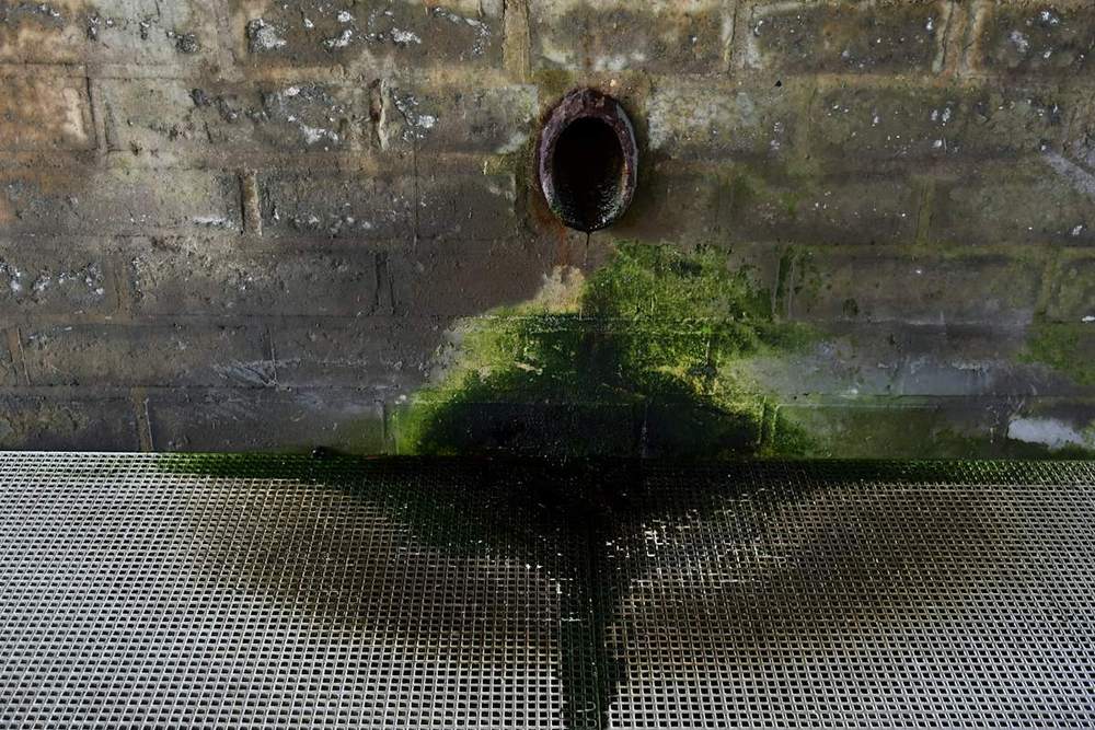 Rusty pipe draining water against a stone wall